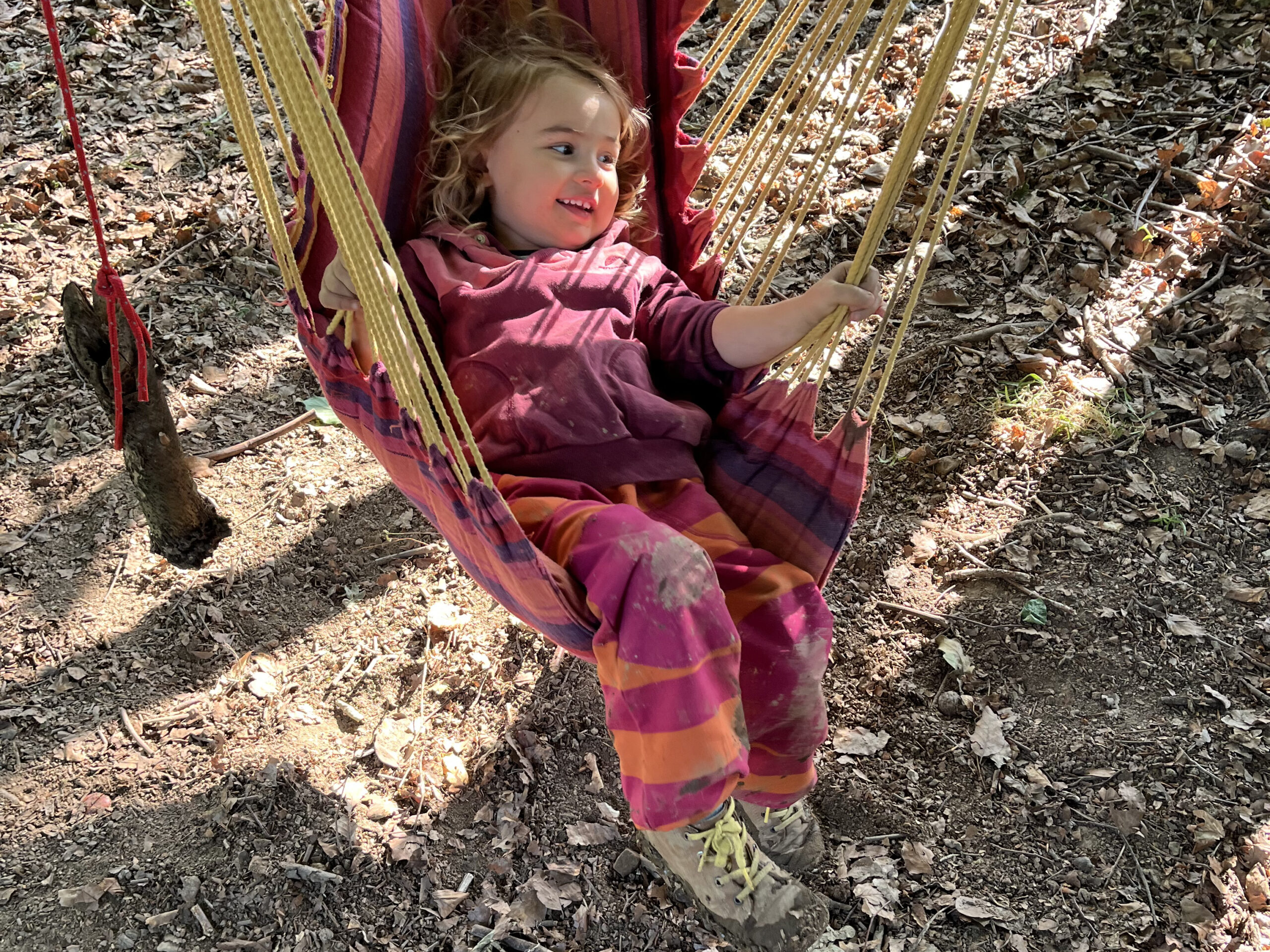 Kind liegt lachend in einer Hängematte im Wald.